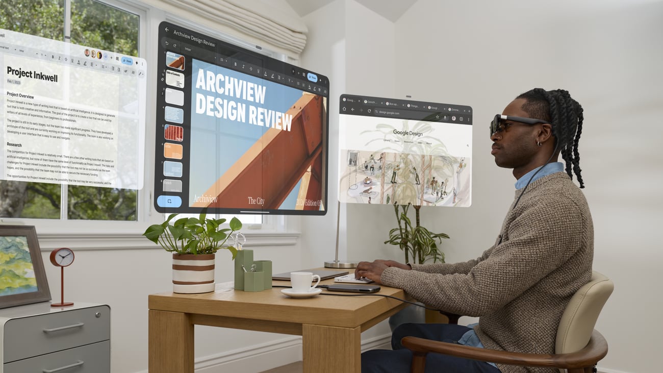 A man at a desk wearing XREAL AURA glasses, with a document, a large design presentation and a browser window floating in the air in front of him